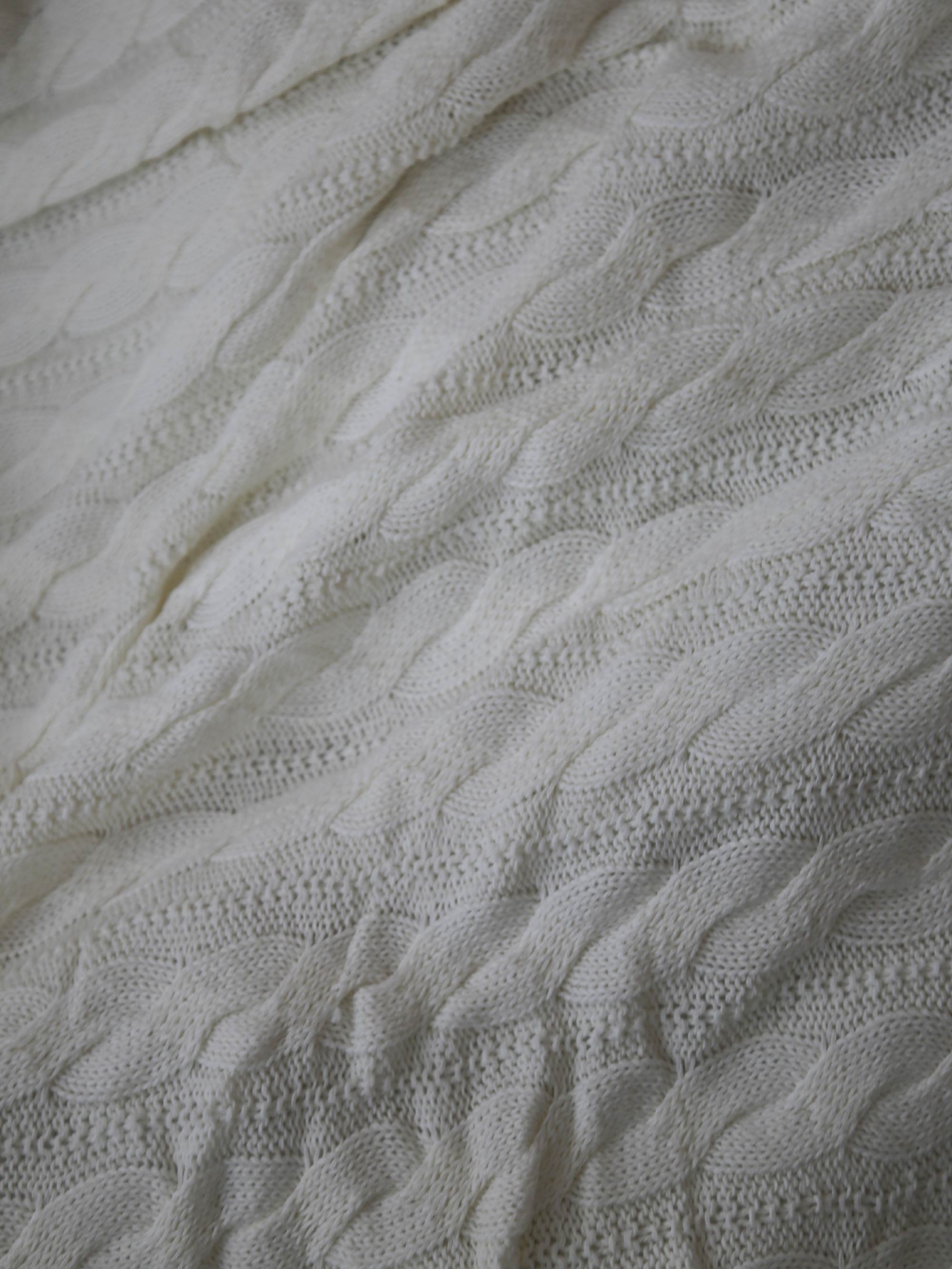 TAKEANAP cable knit cotton throw blanket in ivory on a sofa